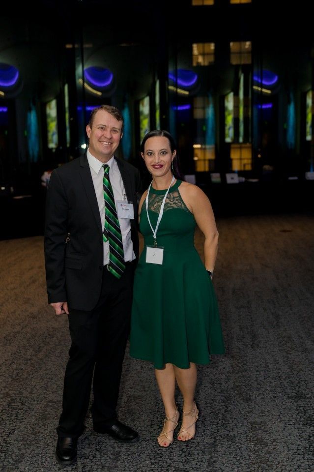 Man in suit with green tie and woman in green dress pose together at an event.