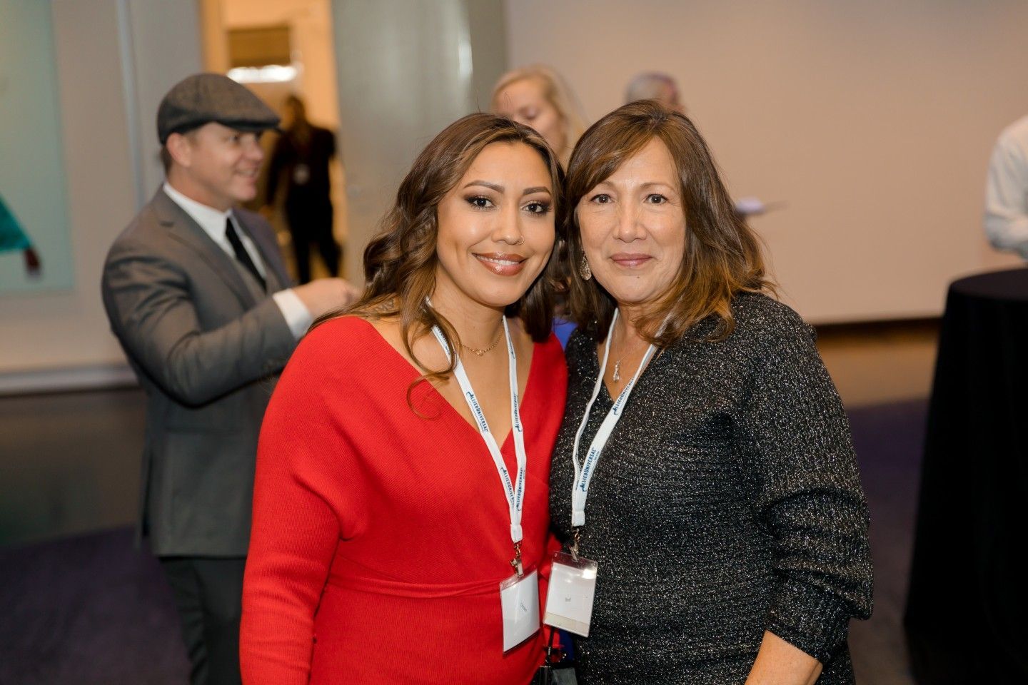 Two women smile, pose together at event; woman in red dress, other in black sequined top.