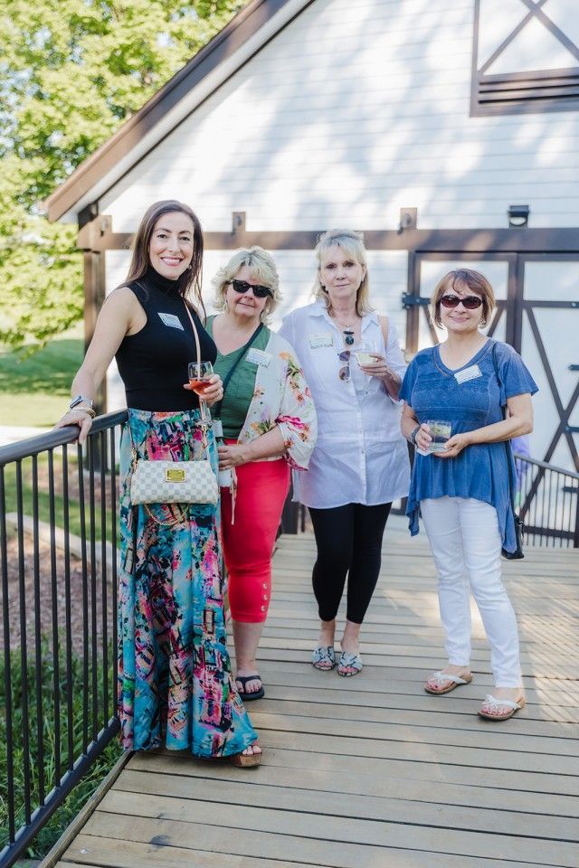 Four people standing on a wooden deck in front of a white building, holding drinks.
