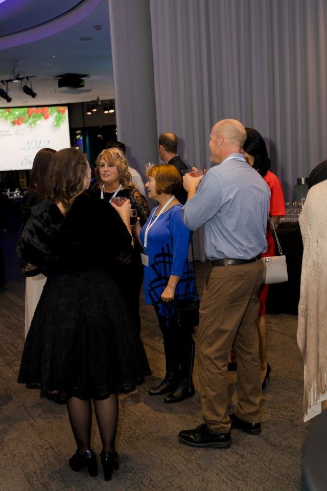 Group of people in a room, some conversing. A woman in blue is talking. Modern interior with lights.