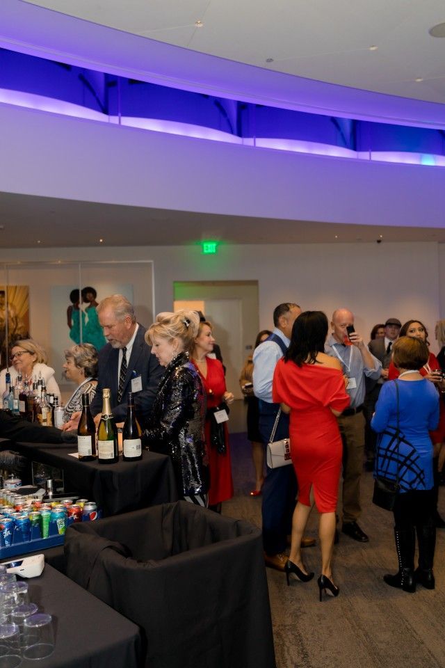 People socializing at a bar in a brightly lit room with blue overhead lighting.