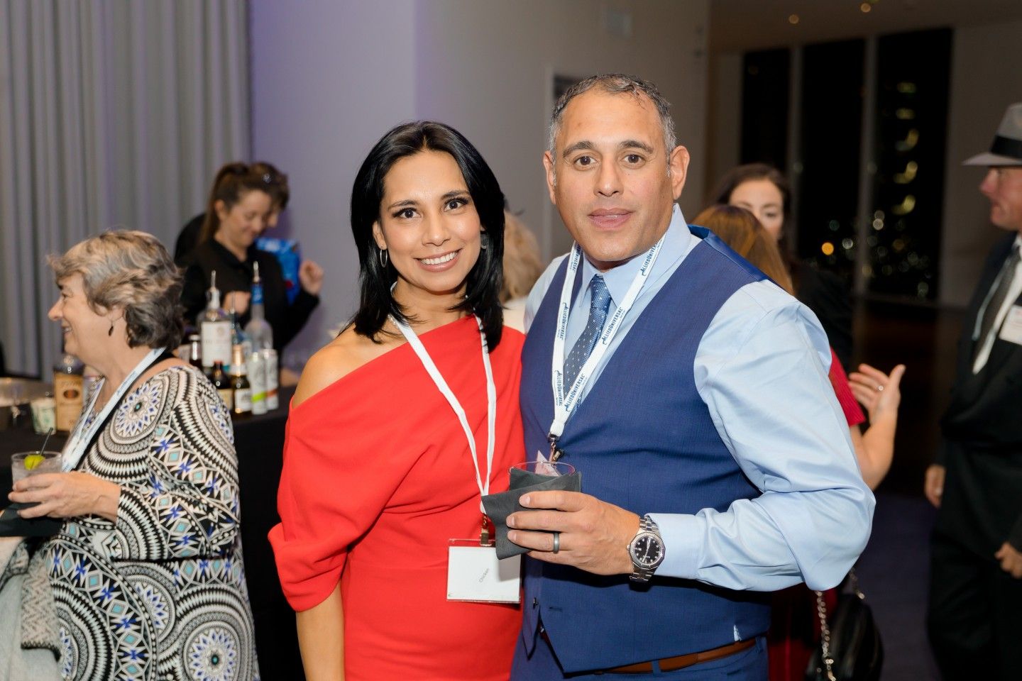 Woman in red dress and man in blue vest smiling at event.