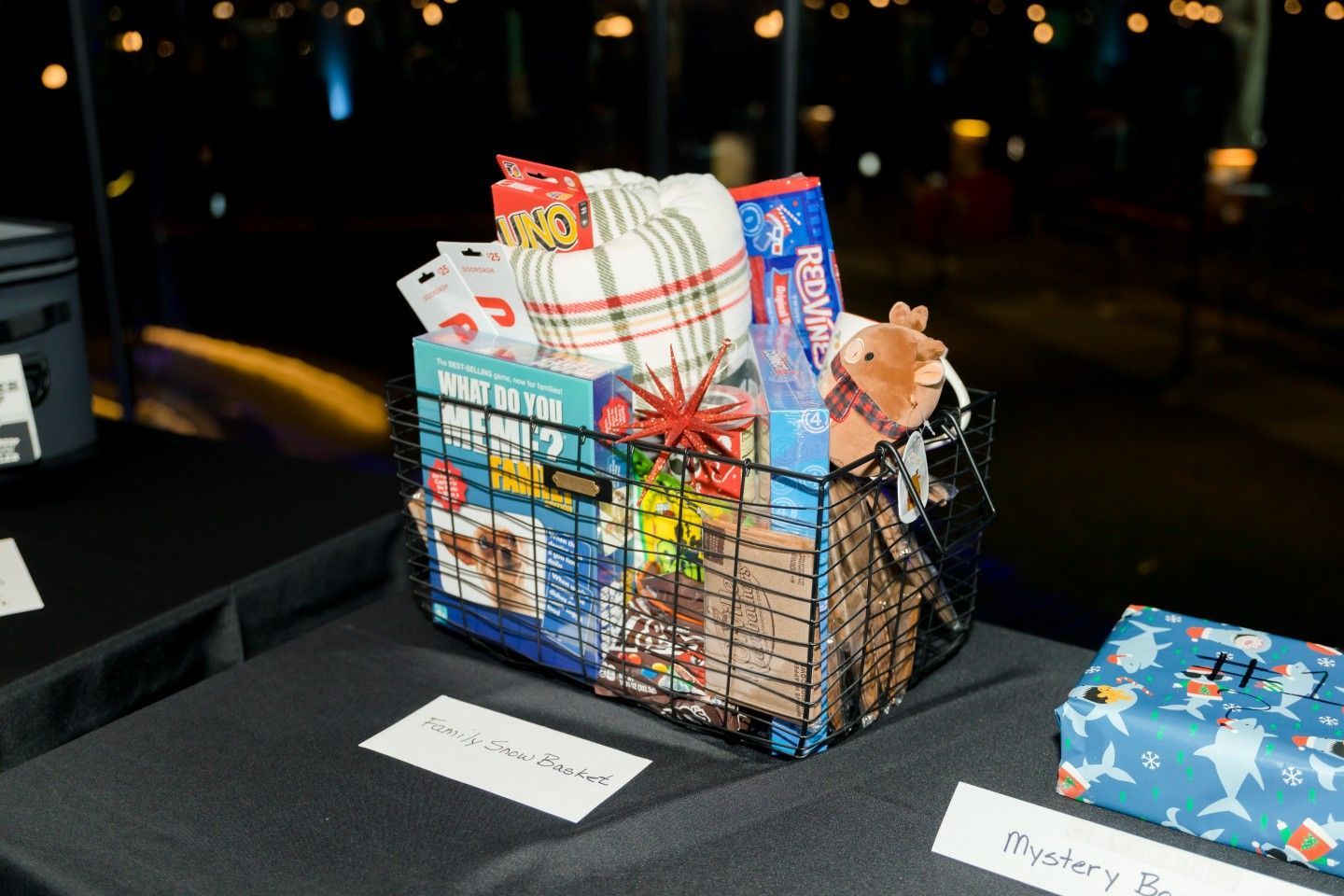 Gift basket filled with snacks, blanket, and plush toy on a table at an event.