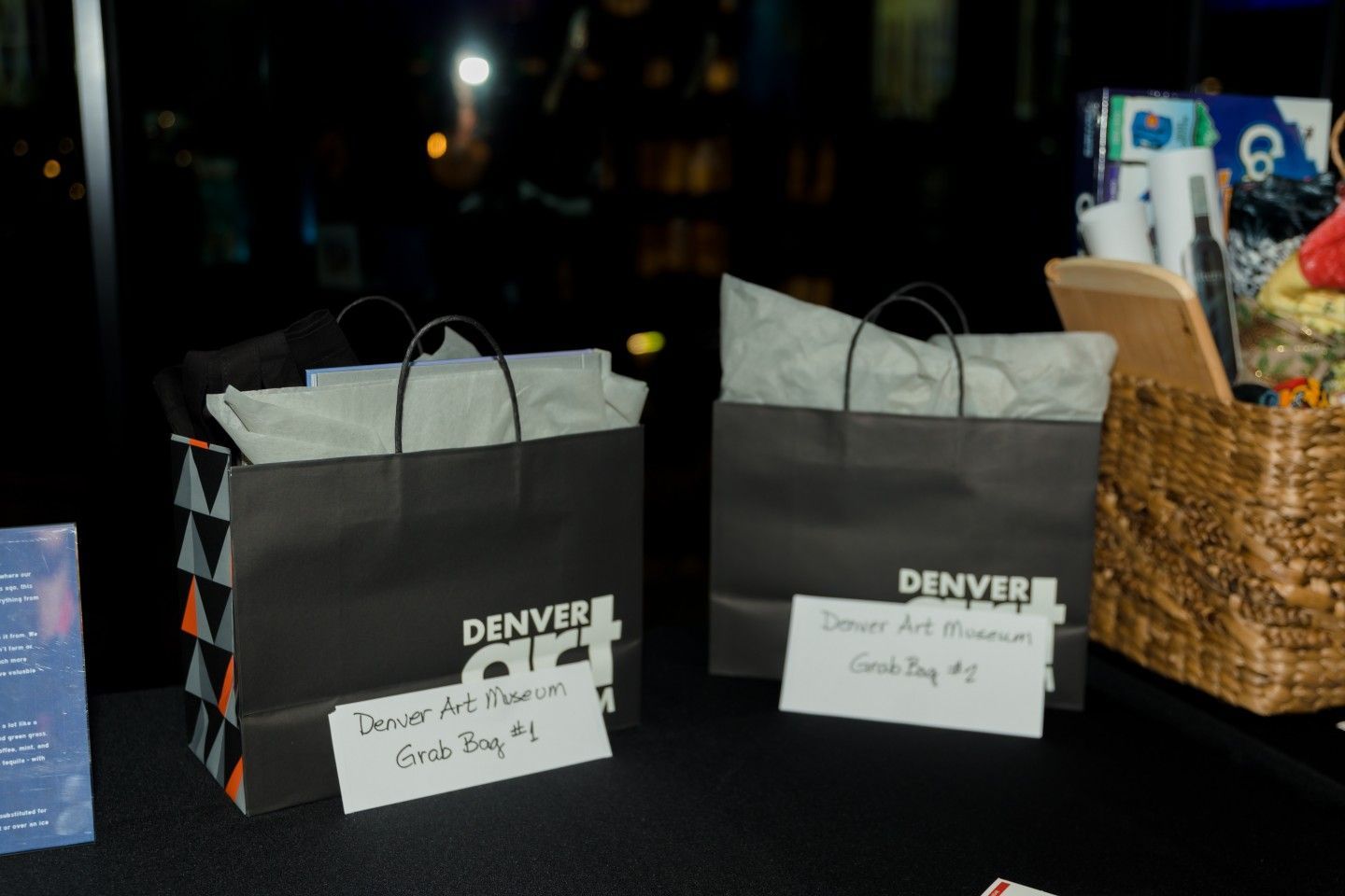 Two black Denver Art Museum gift bags, labeled with numbers, sit on a table.