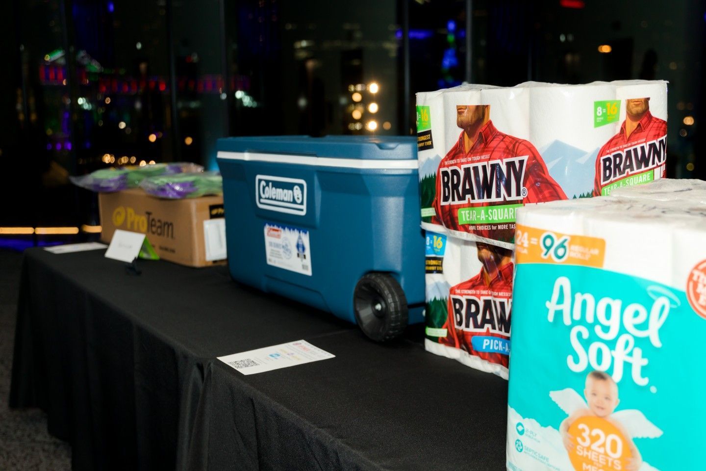 Table with items including a blue cooler, paper towels, and other supplies at an event.