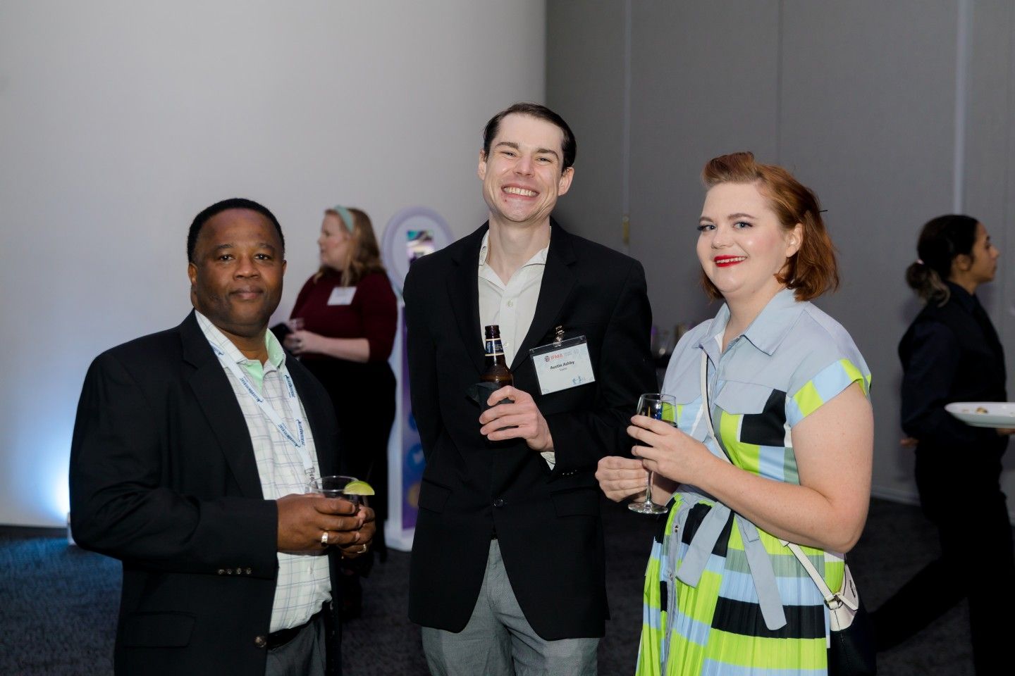 Three people smiling, holding drinks, at a networking event.