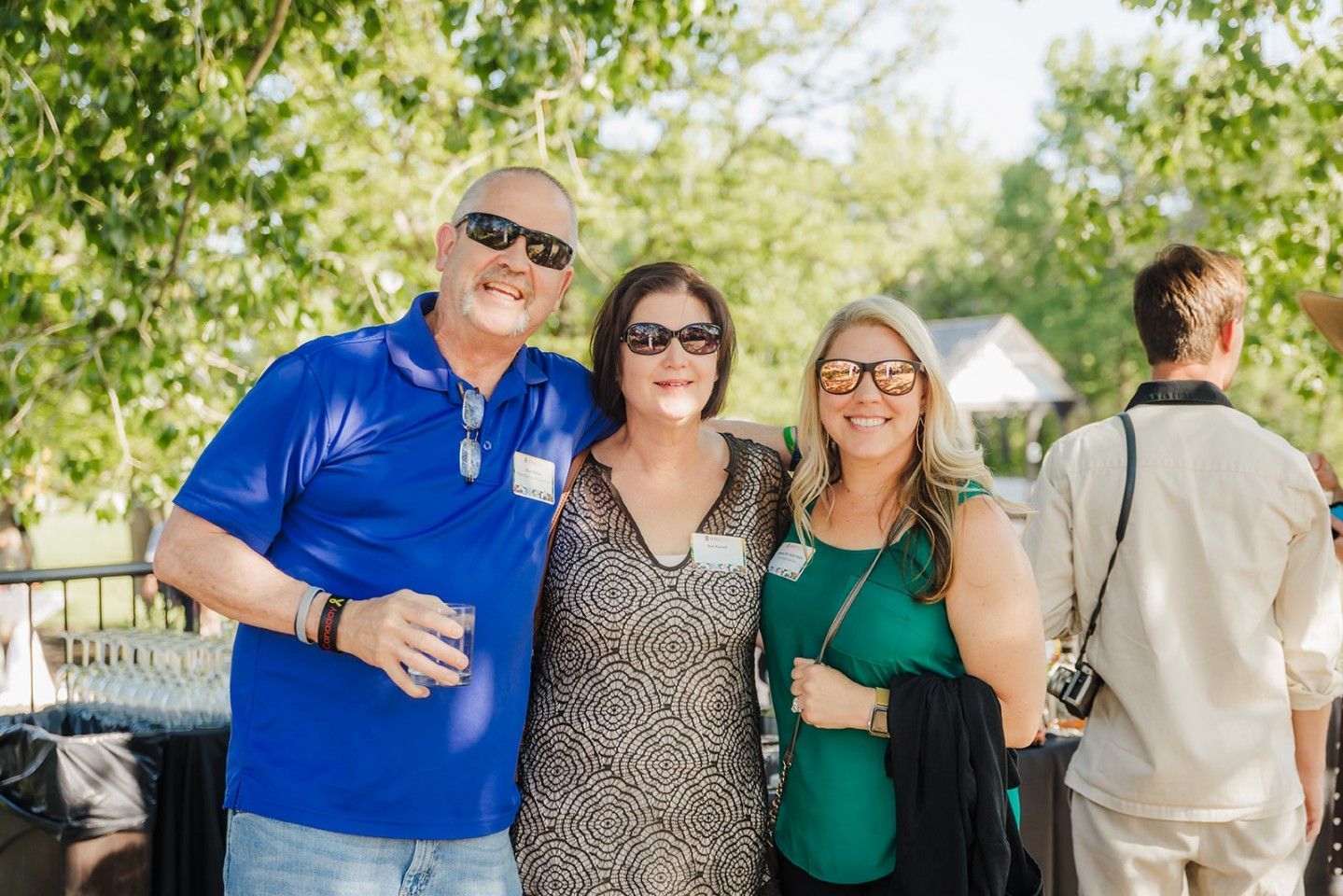 Three people smiling, wearing sunglasses, standing outdoors.