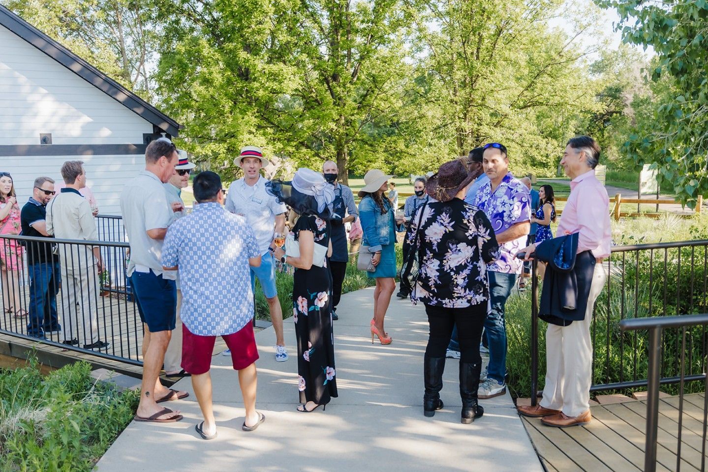 Guests socialize outdoors on a walkway near a building and greenery.