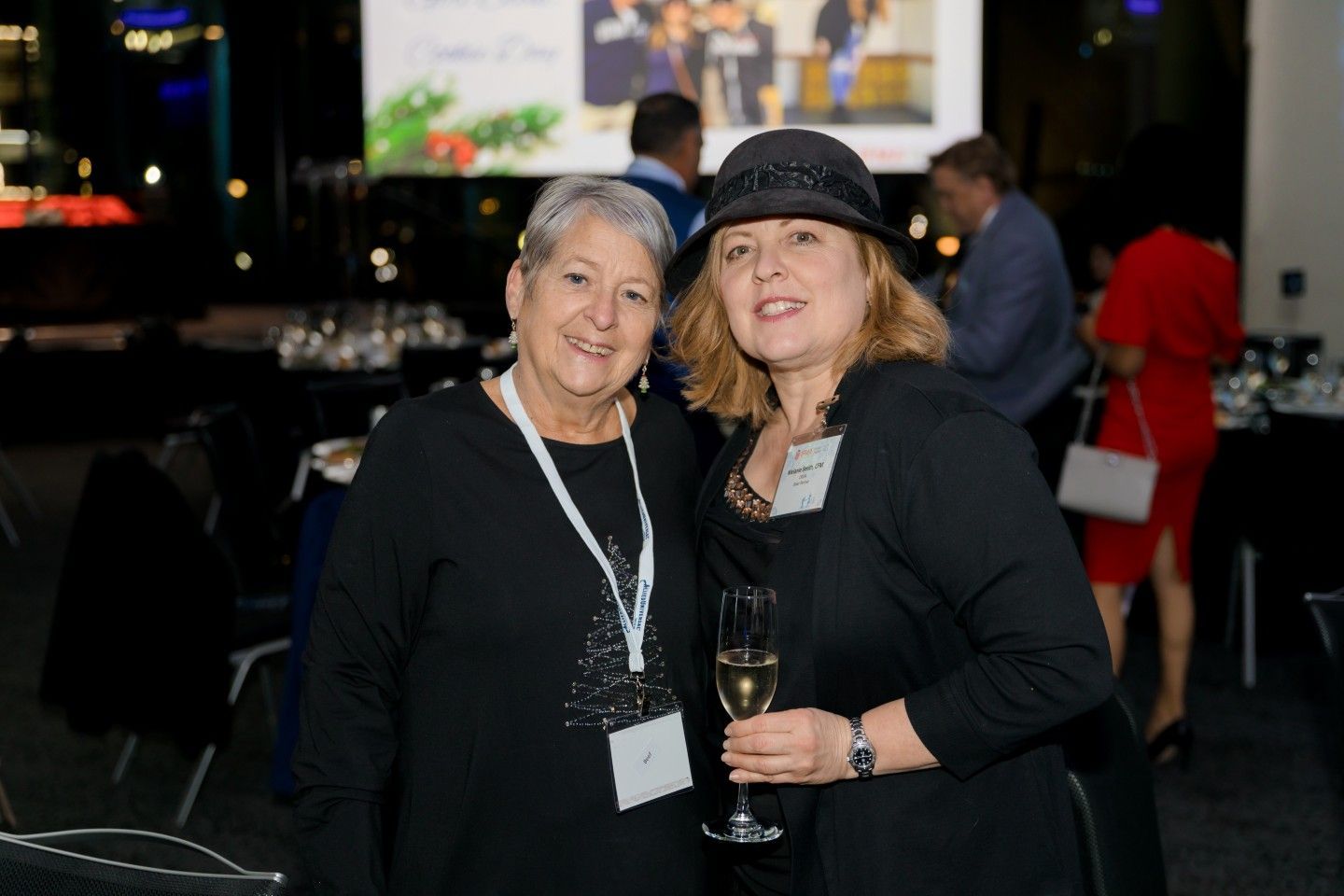 Two women smiling at an event, one holding a glass of champagne.