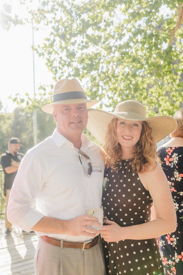 Couple in hats smiling, outdoors. Man in white shirt, woman in polka dot dress.