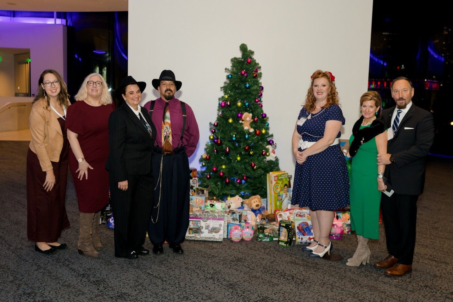 Group of people in festive attire posing near a Christmas tree with presents.