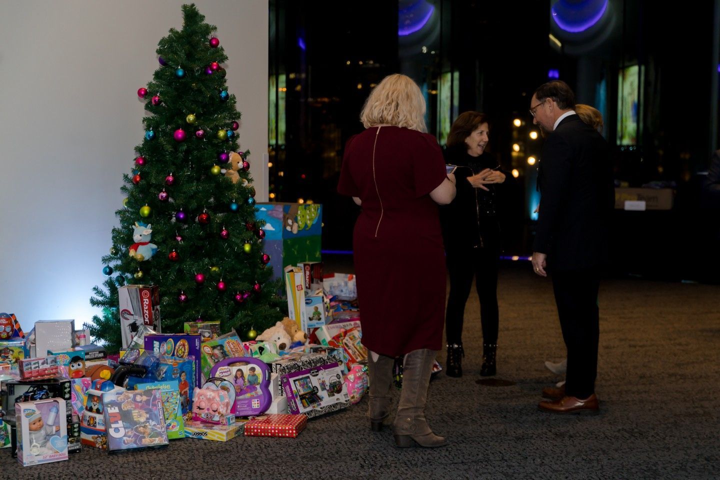People near a Christmas tree surrounded by wrapped gifts.