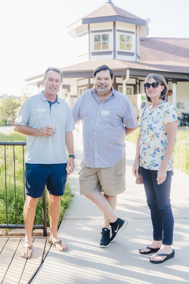 Three people pose outdoors near a building.