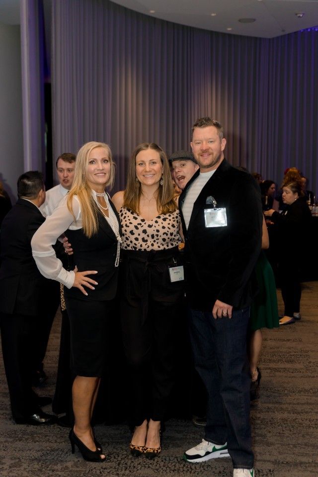 Three people smiling at an event: blonde woman in black suit, woman in a patterned top, man in a blazer.