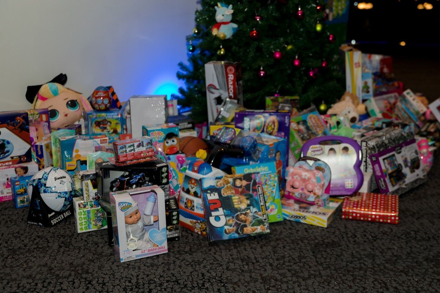 Christmas presents piled on carpet in front of a decorated tree with lights and ornaments.