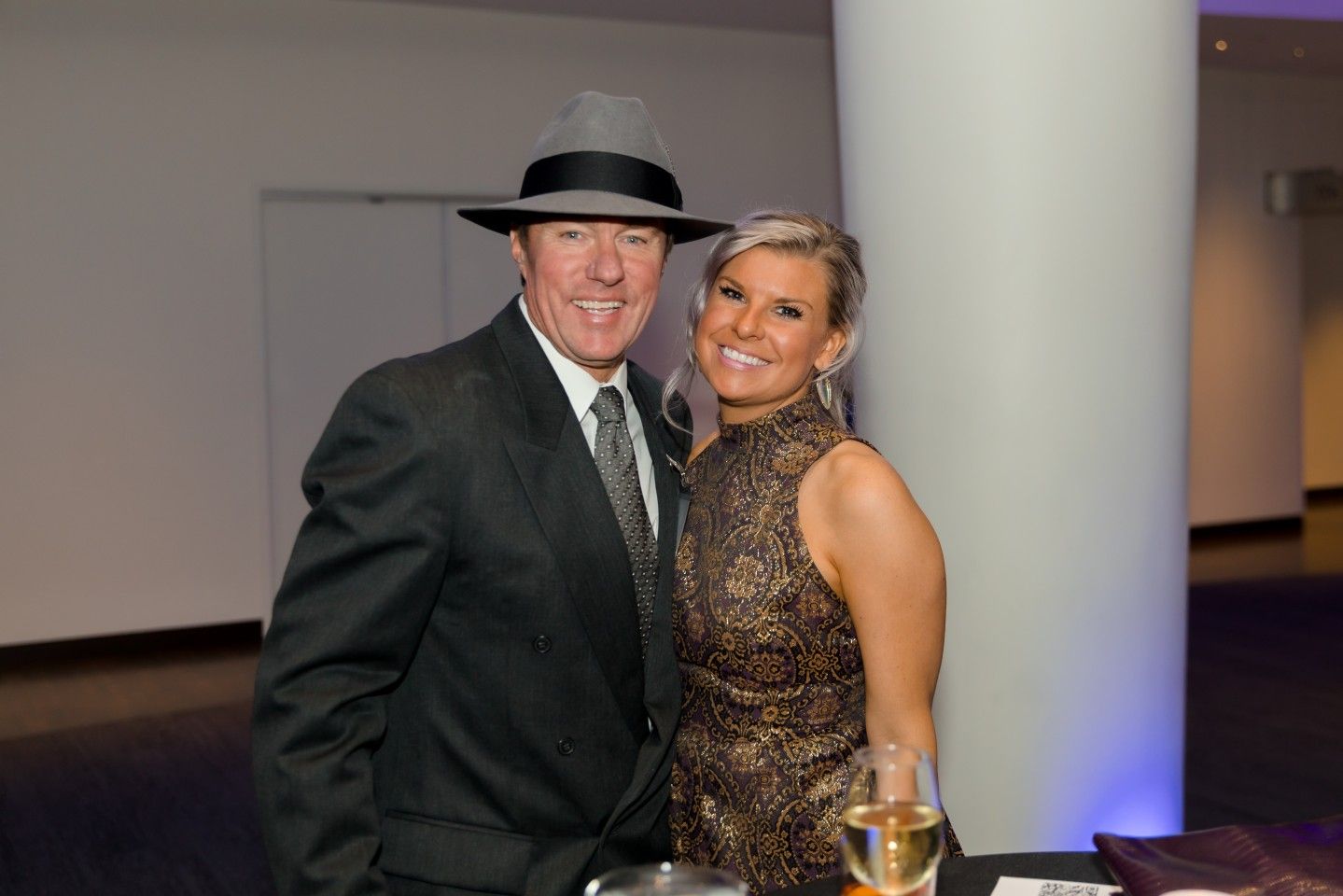 Man in suit and fedora with woman in gold dress, smiling and posing together.