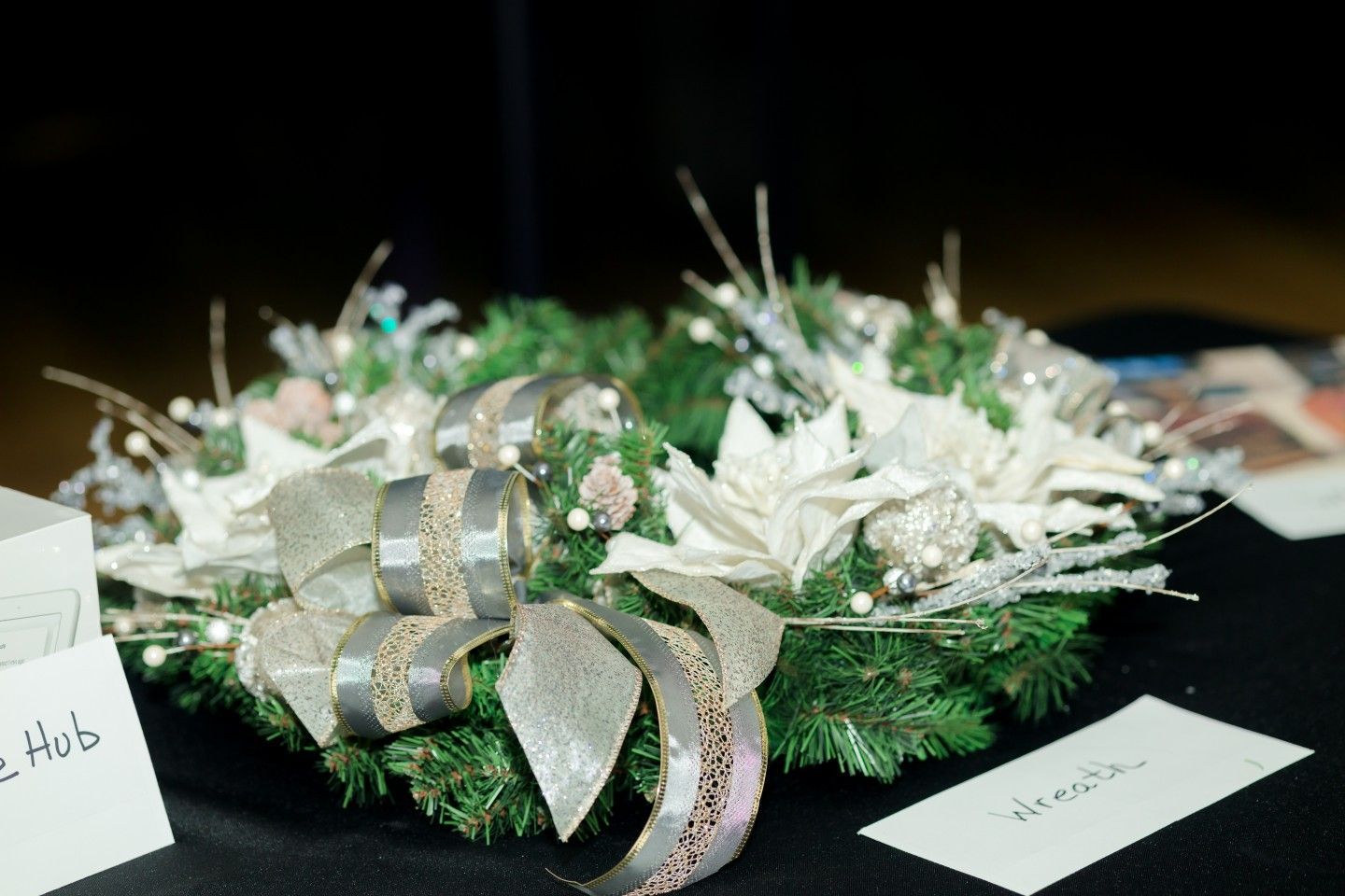 Christmas wreath with silver bow and decorations on a black surface.