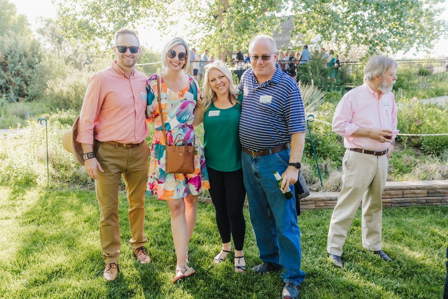 Four people smiling and posing outdoors. Green grass, trees in background.