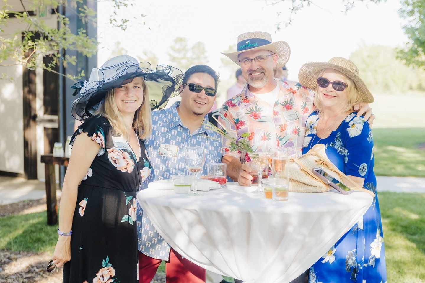 Four people in festive attire pose around a small table outdoors.
