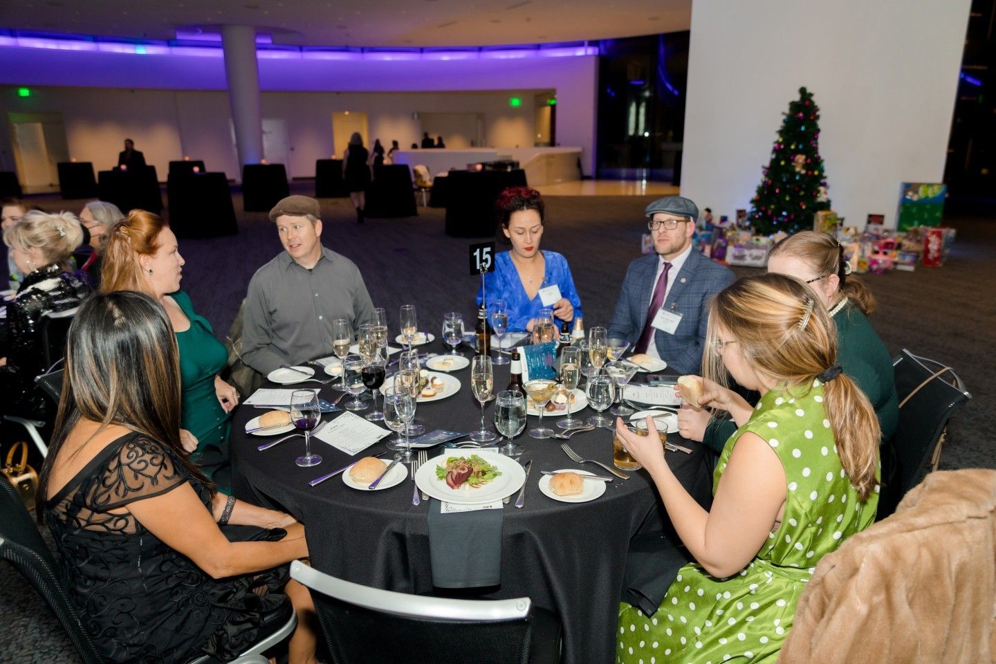 People seated at a round table, eating and conversing; festive decorations are in the background.