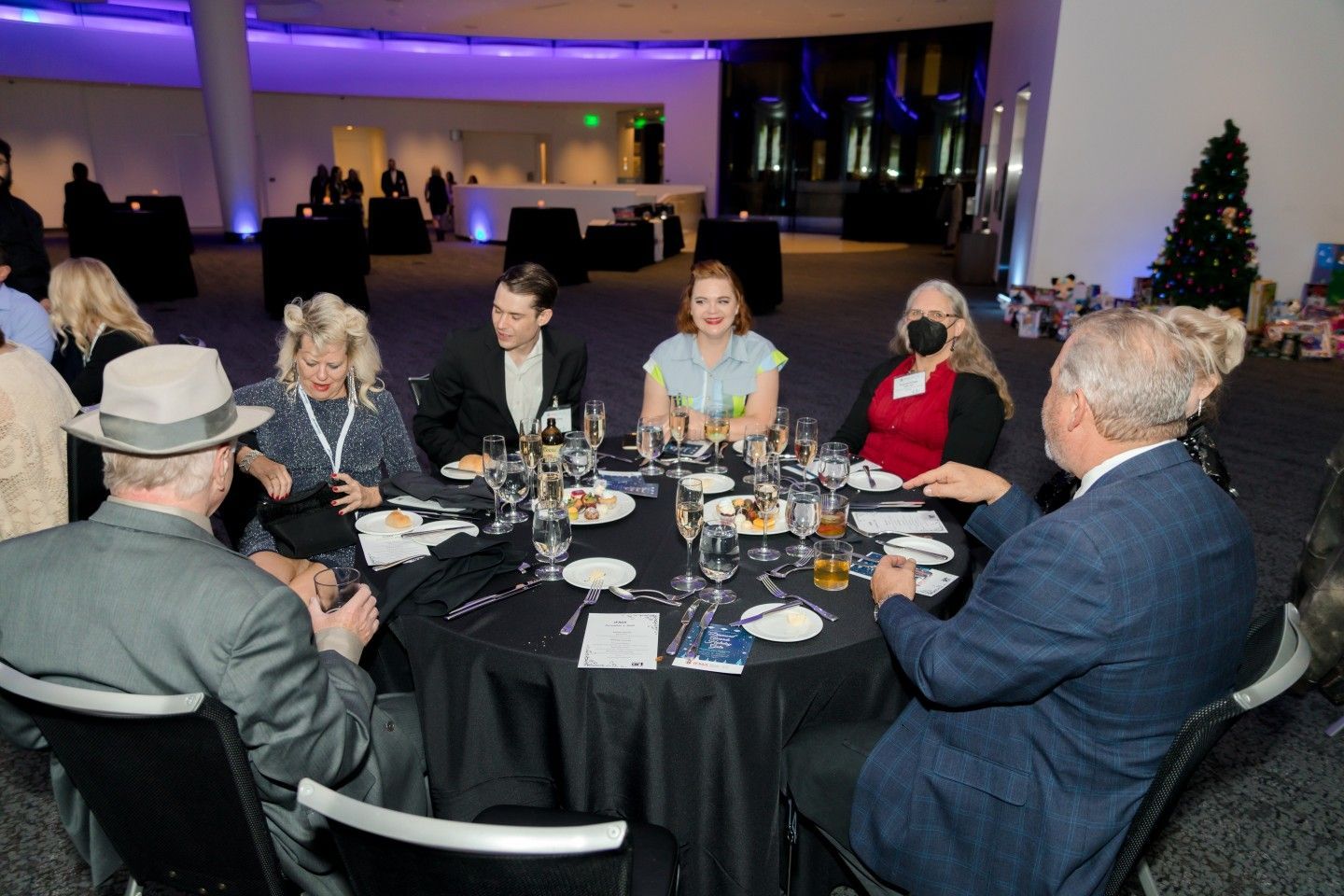 People seated around a black table at an event, with food and drinks.