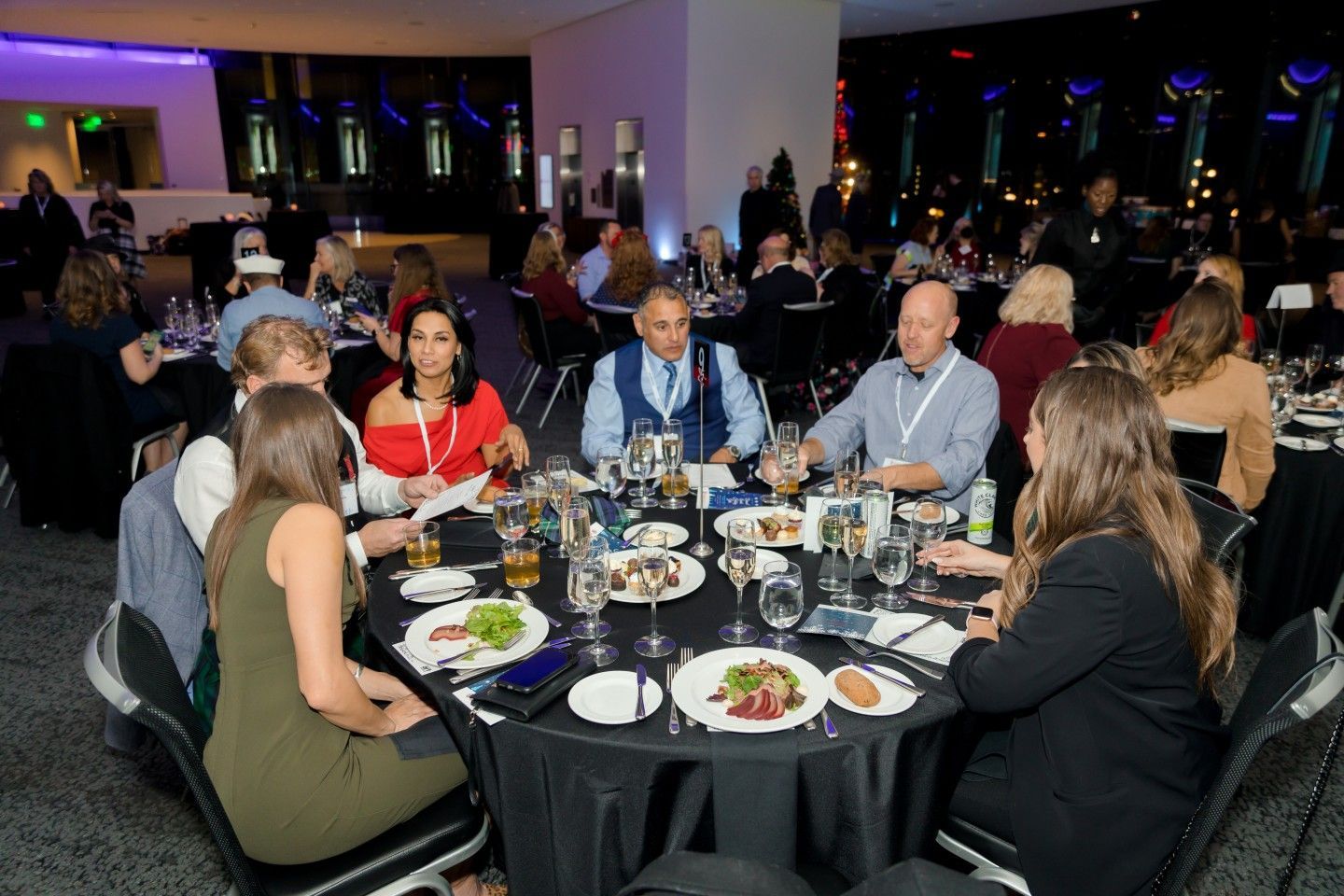 People seated at round tables in a dimly lit event space, eating and conversing.