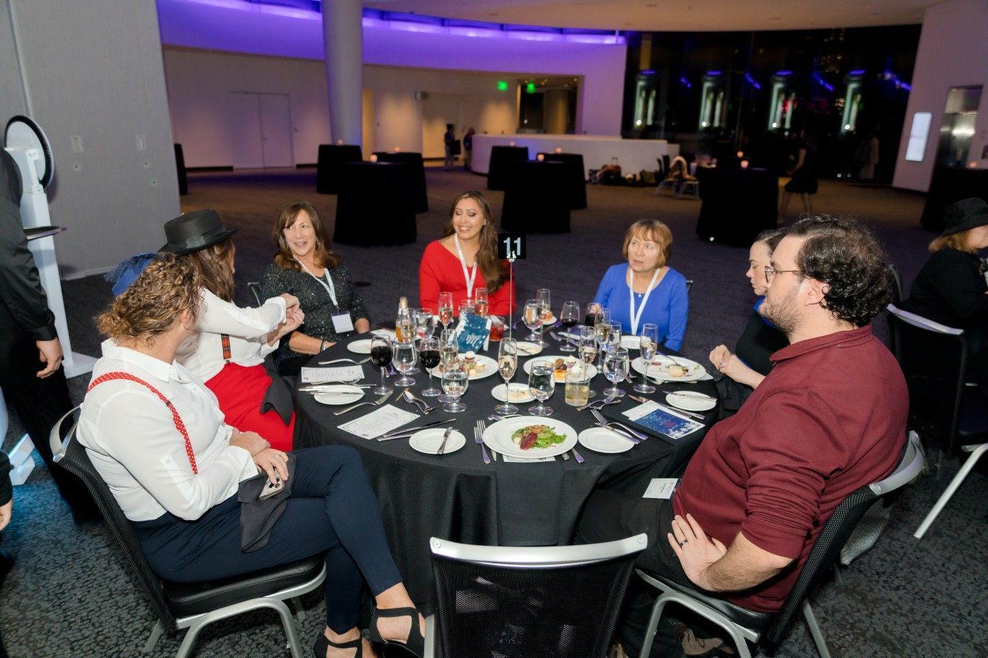 People seated at a round table, eating dinner in a dimly lit event space.
