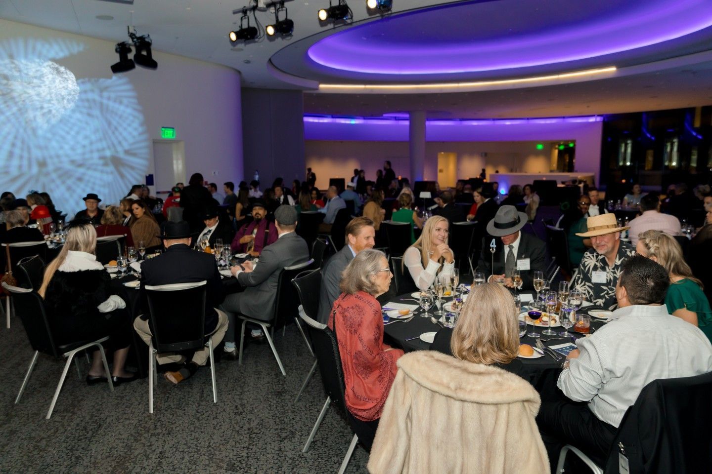 People seated at round tables in a large, brightly lit event space with a curved ceiling.