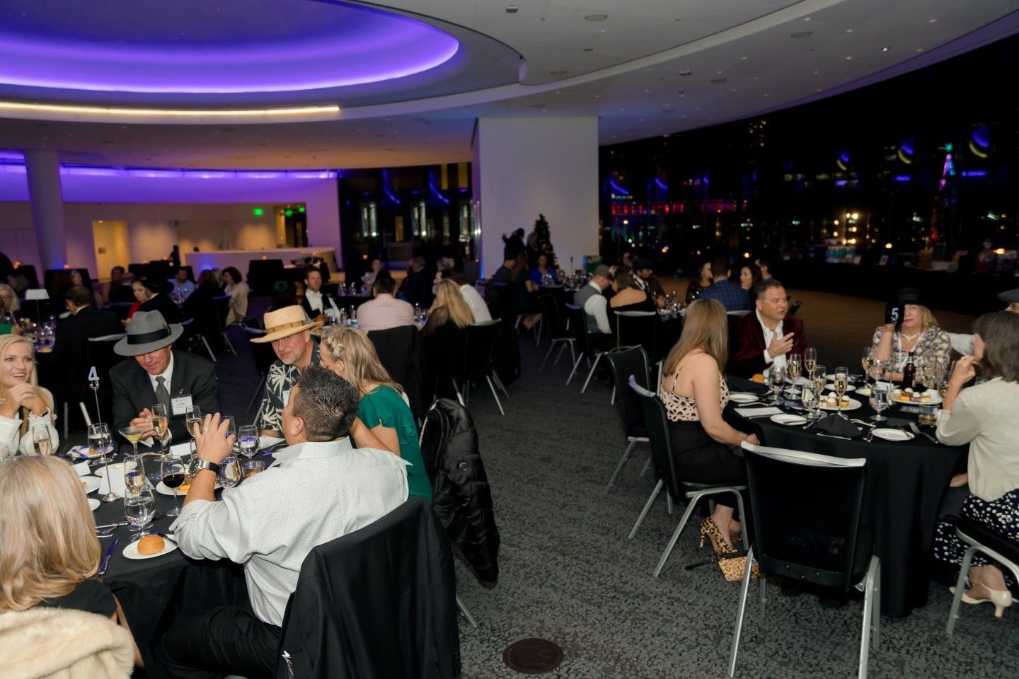 People seated at tables in a brightly lit room with city lights visible outside.