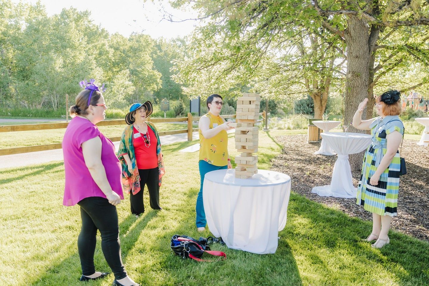 People playing giant Jenga game in a grassy park, a tree in background.