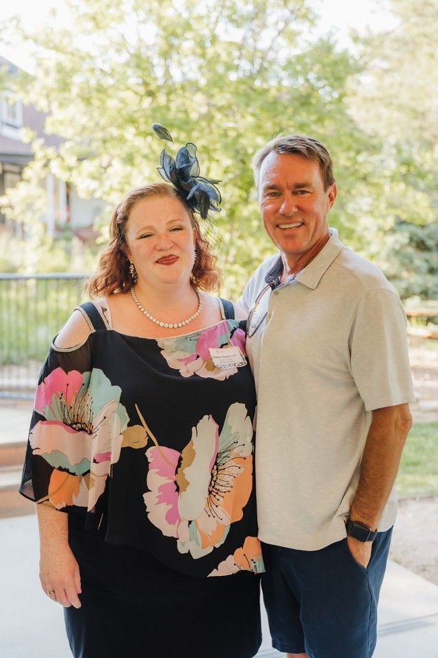 Woman in floral top with man in polo shirt posing outside.
