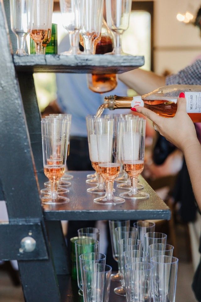 Person pouring rose-colored champagne into fluted glasses on a tiered serving stand.