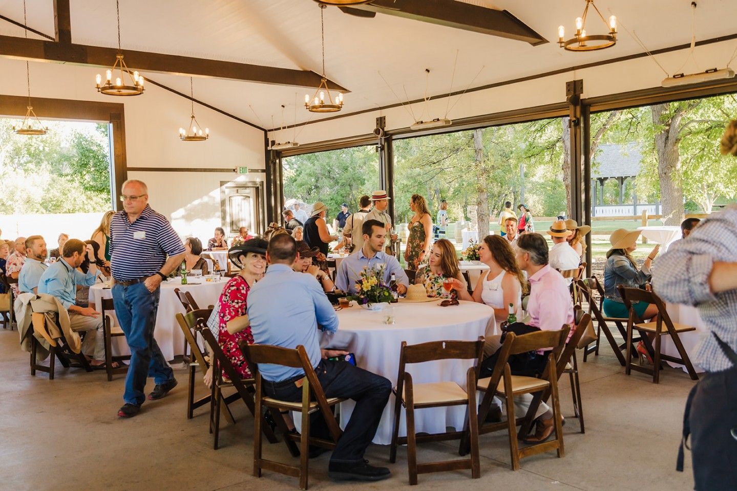 People seated at tables inside a light-filled pavilion with open sides; many guests mingle.