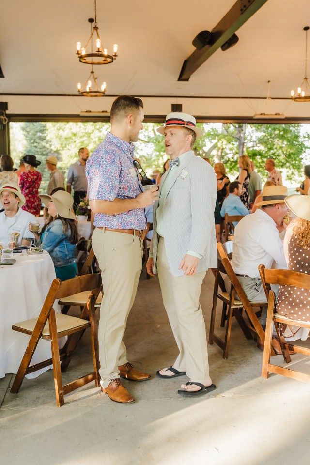 Two men in summer attire converse at an outdoor event with tables and guests.