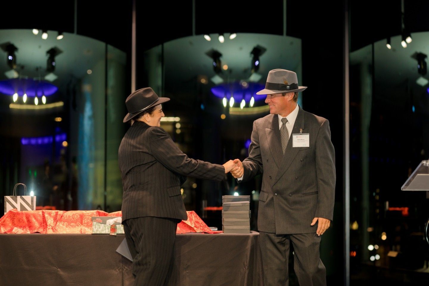 Two people in suits and hats shaking hands onstage.