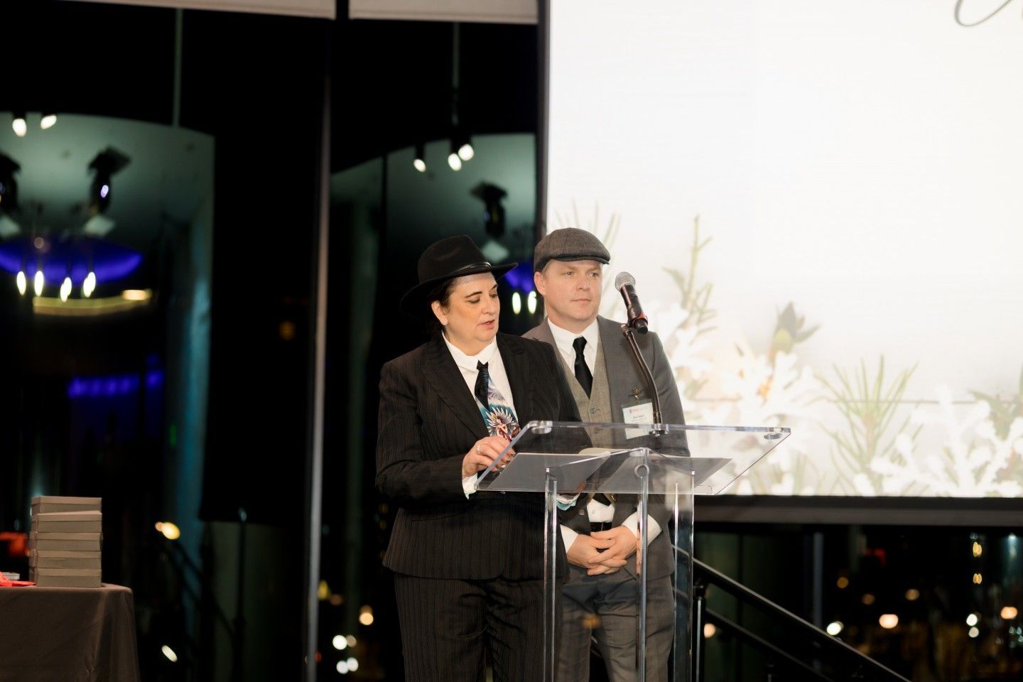 Two people in suits at a podium, holding an award. Event backdrop.