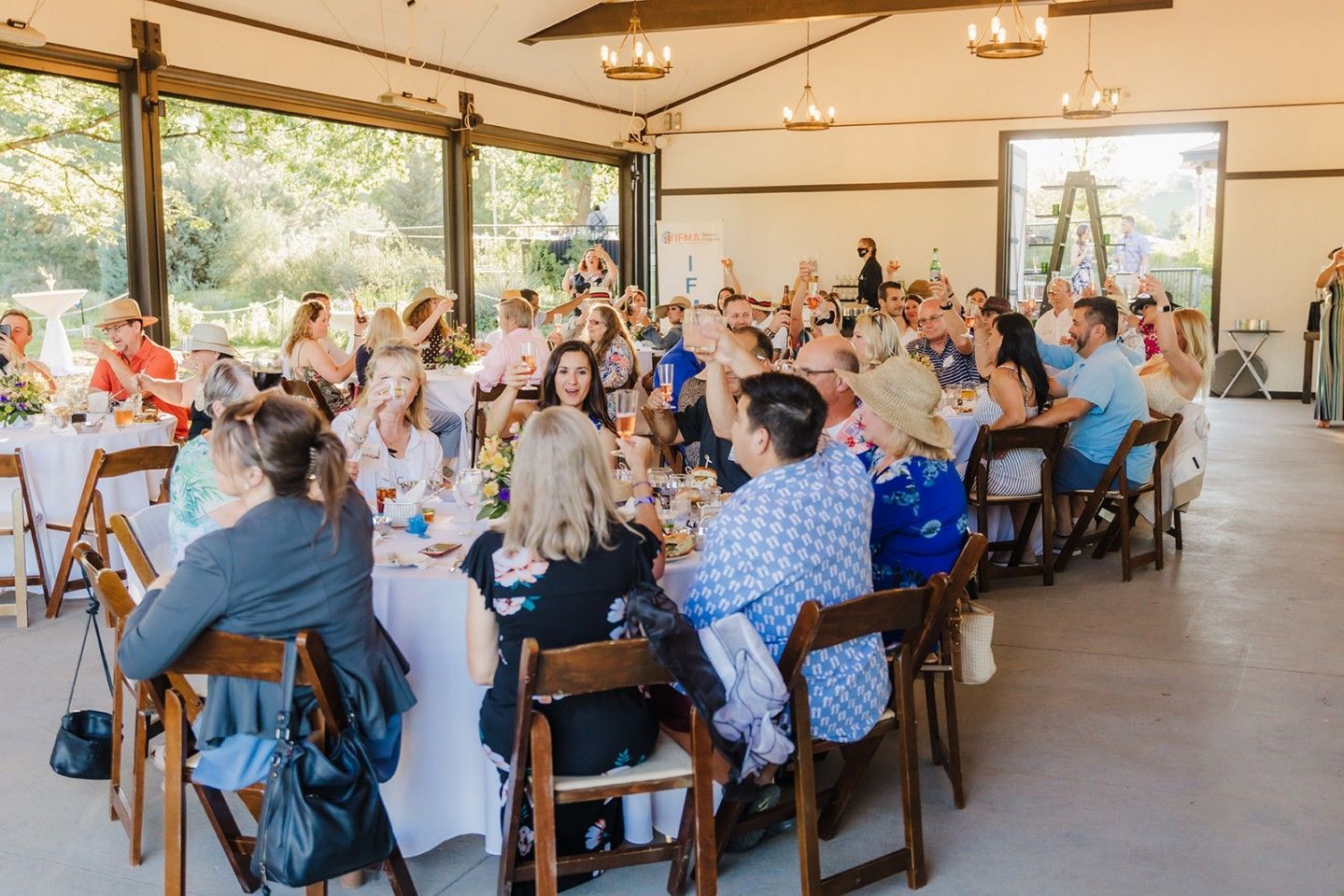 People seated at tables inside a building with large windows, possibly an event or celebration.