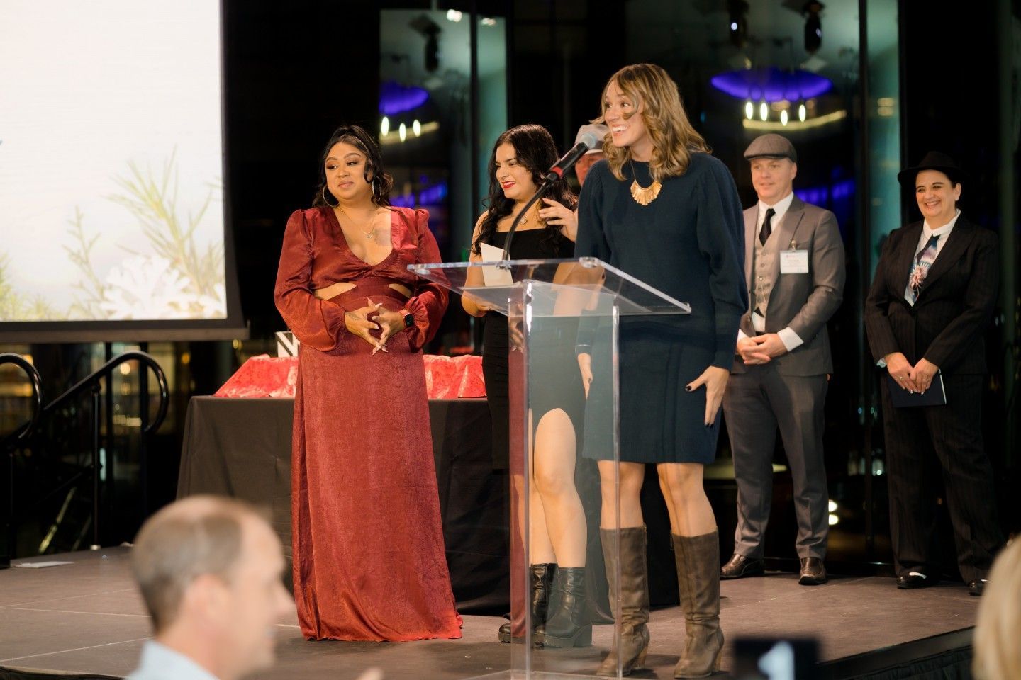 People at podium; woman in blue speaks, others stand by. Awards event.