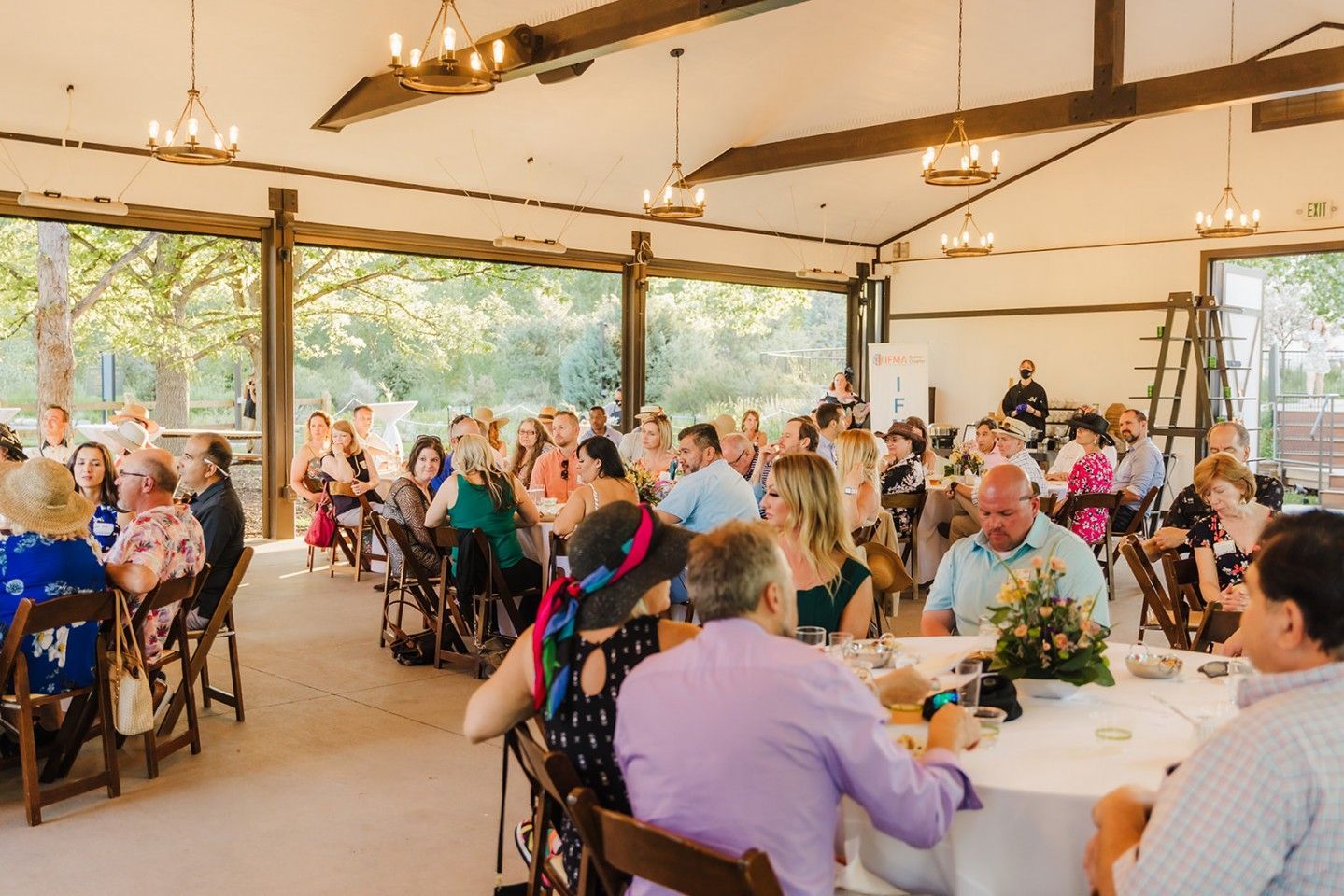 People seated at tables inside a large open-air building, attending an event.