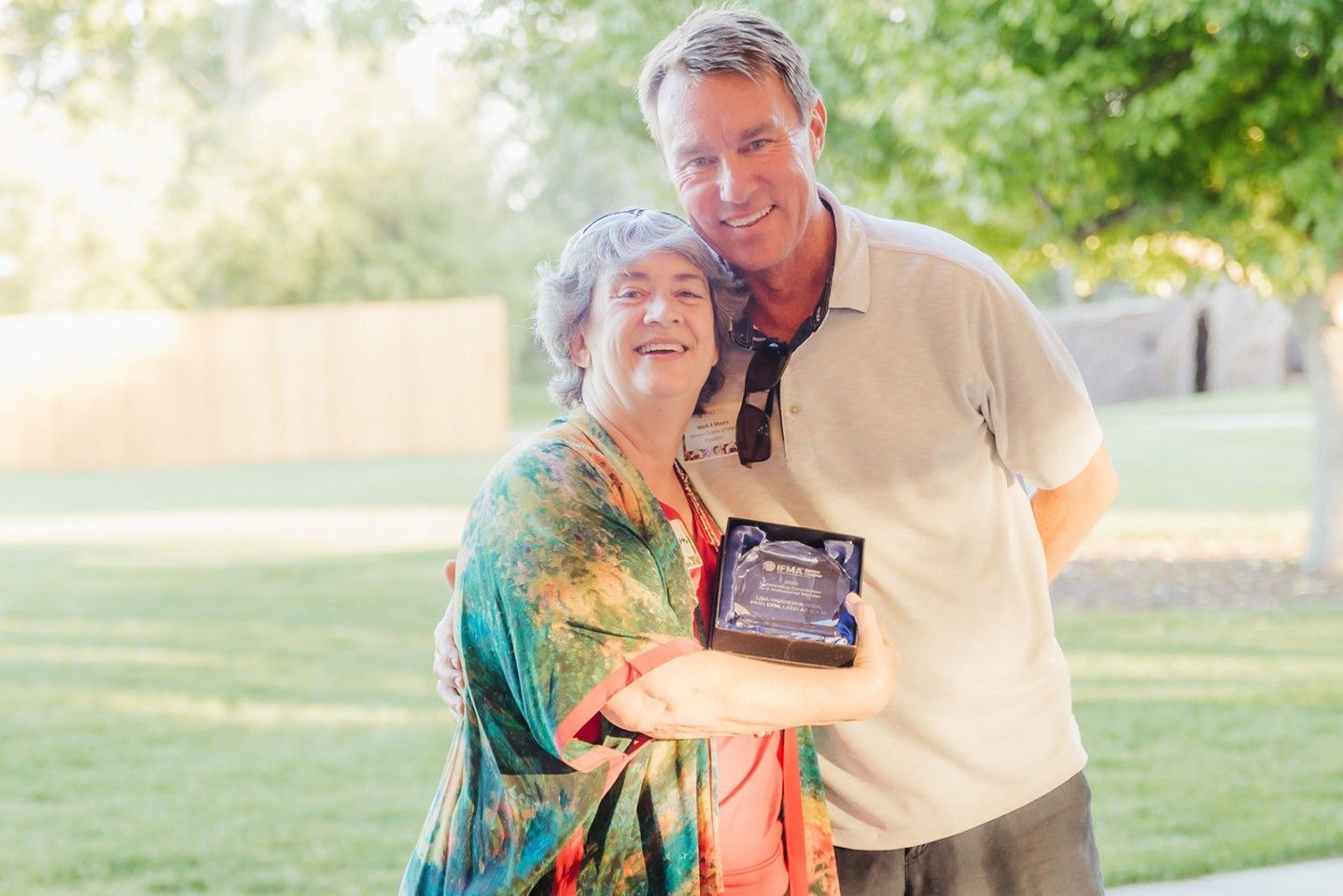 Man and woman outdoors, smiling, embracing, holding a small device.
