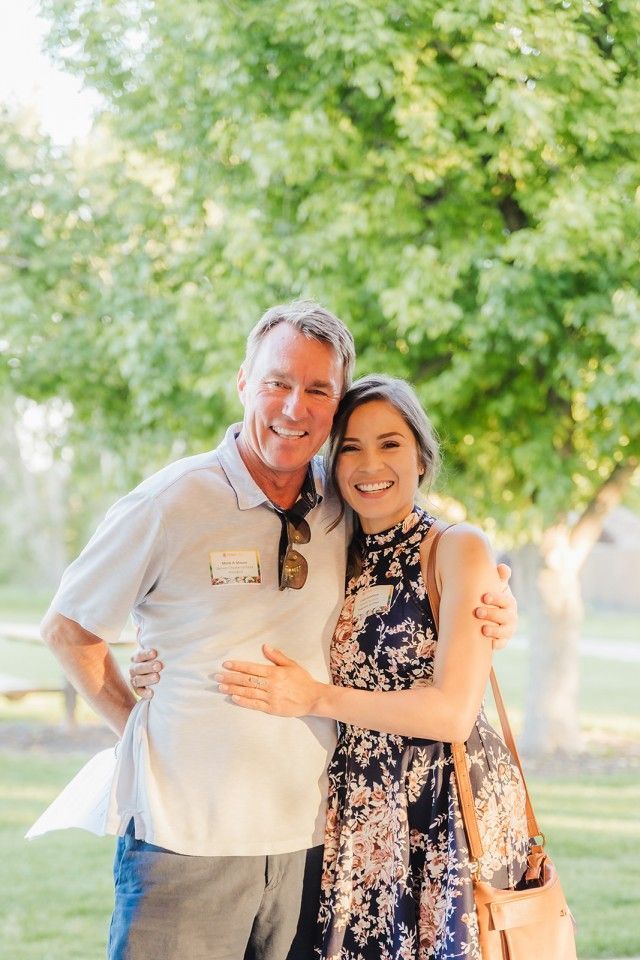 Man and woman with arms around each other, smiling. They stand outside in front of a tree.