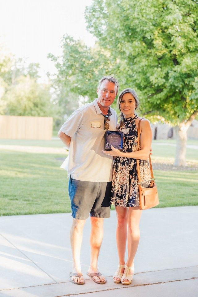 Man and woman posing outdoors, holding a plaque.