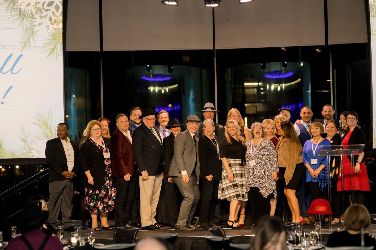 Group of people on a stage celebrating, with festive décor, and a screen in the background.