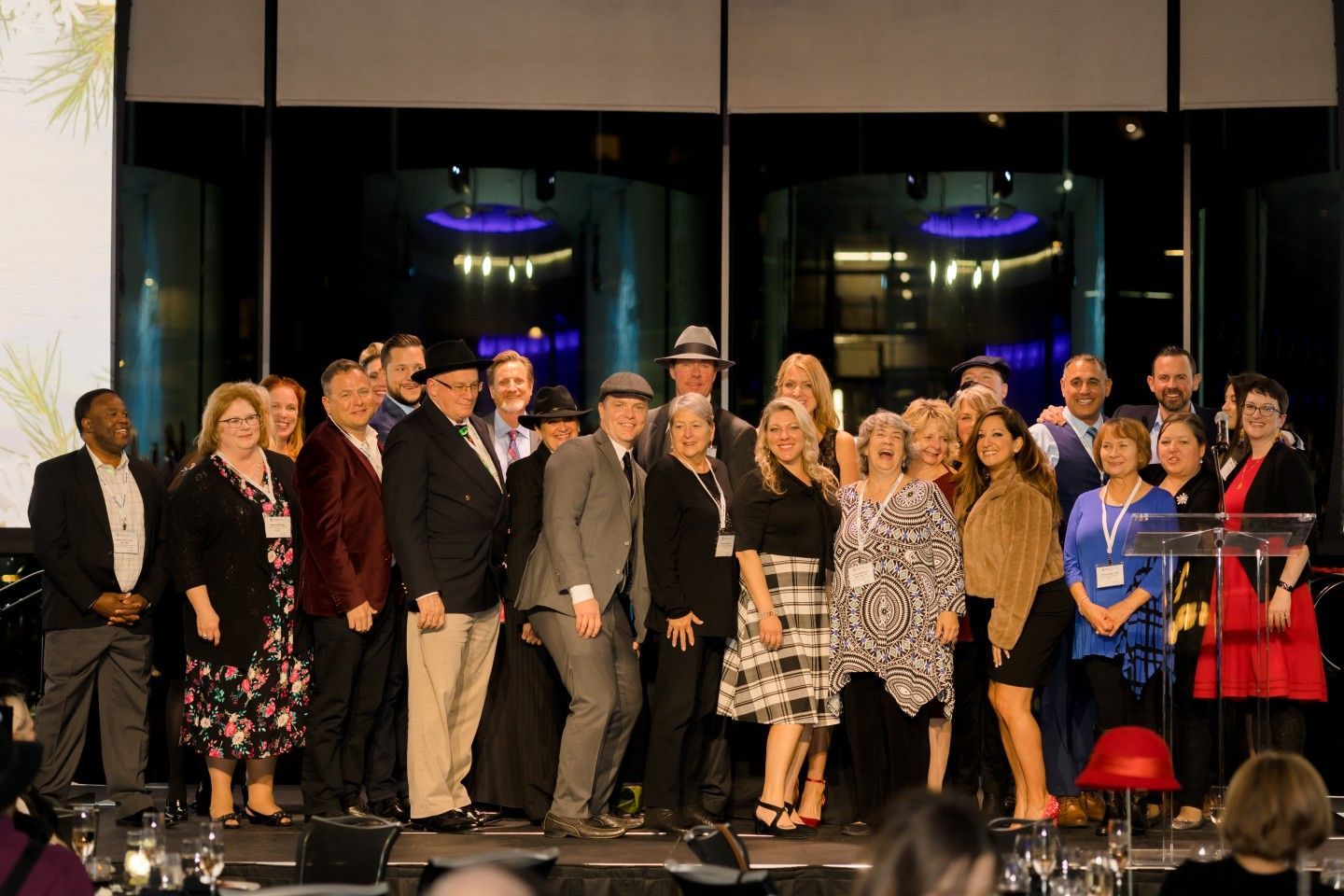 Group of people on stage, some smiling, in front of a mirrored wall with lights.