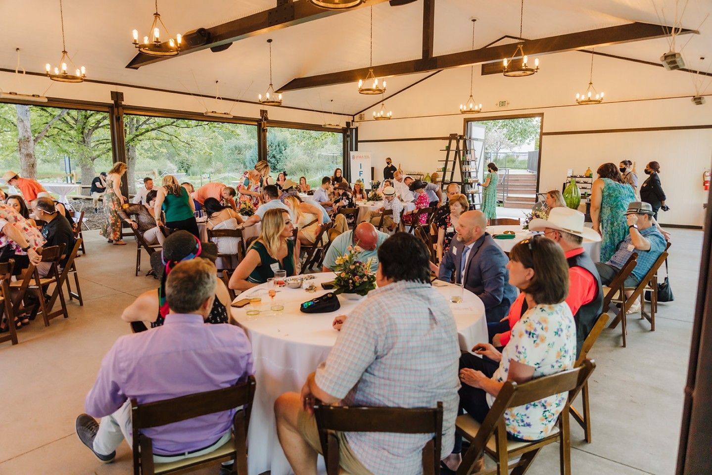 People gathered at an outdoor event under a covered pavilion, seated at tables and socializing.