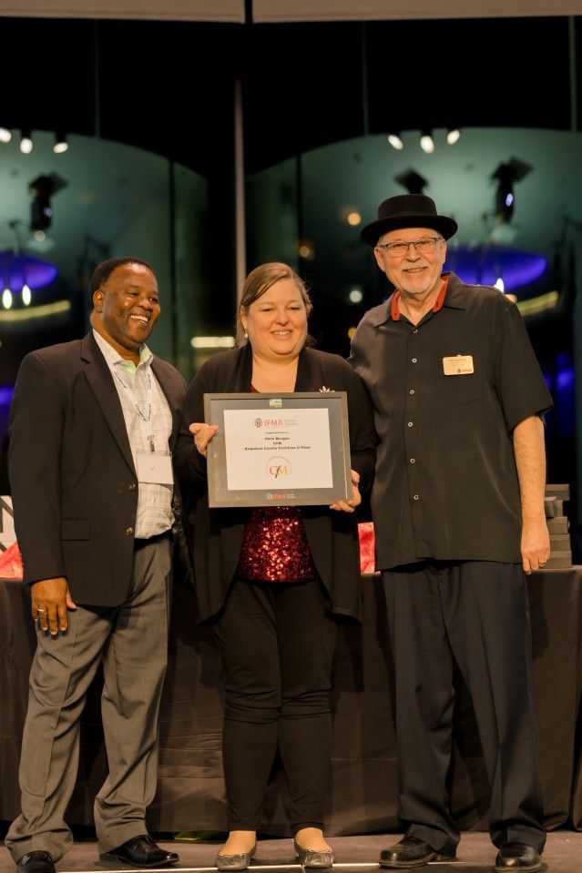 Three people on stage holding an award. Woman in the center. Background is blurry.