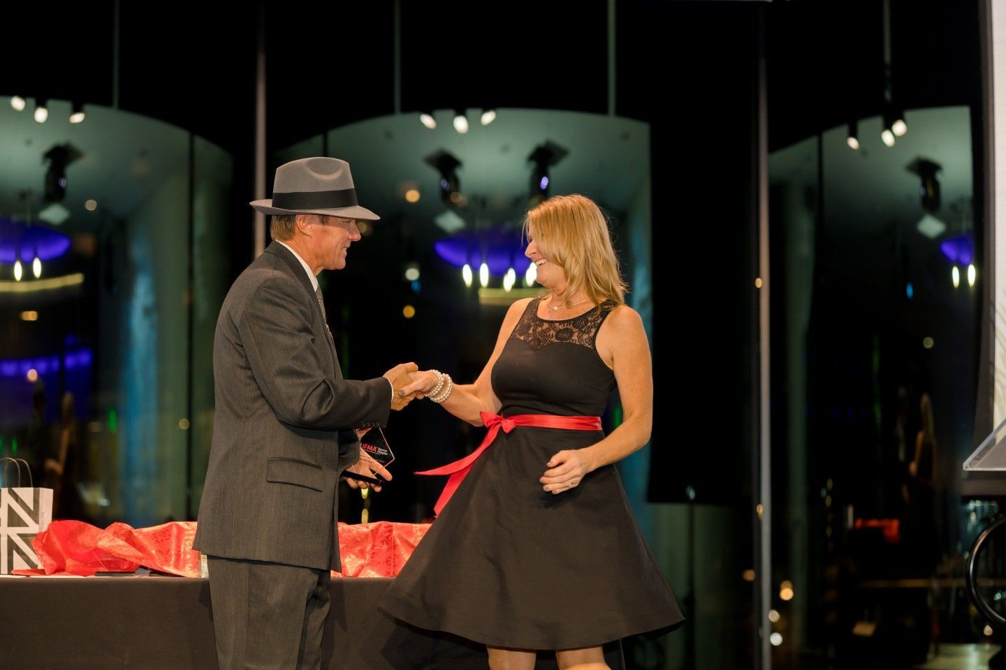 Man in suit shakes hands with woman in black dress on stage.