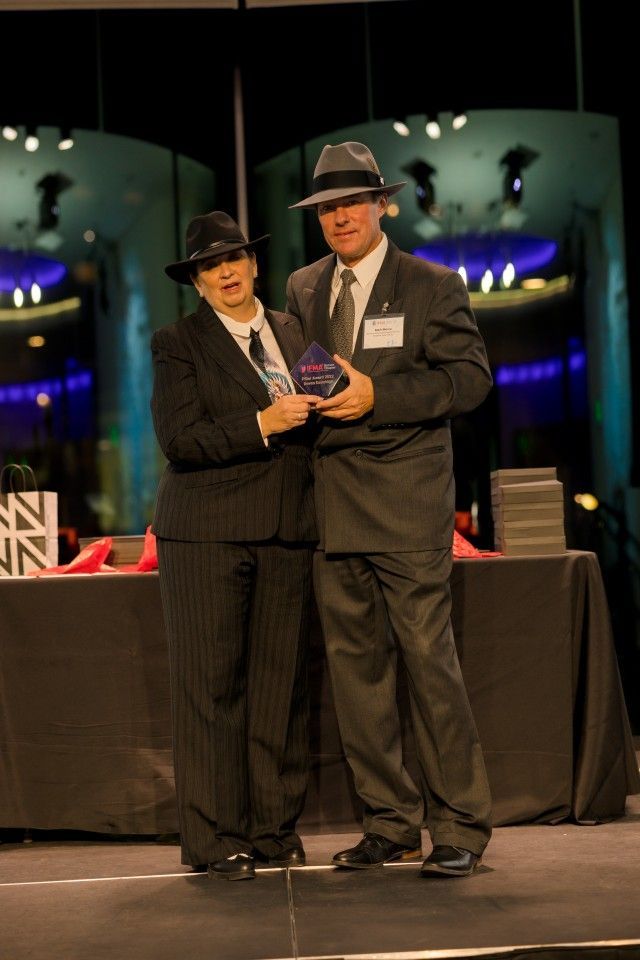 Two people in suits and fedoras on a stage, holding an award.