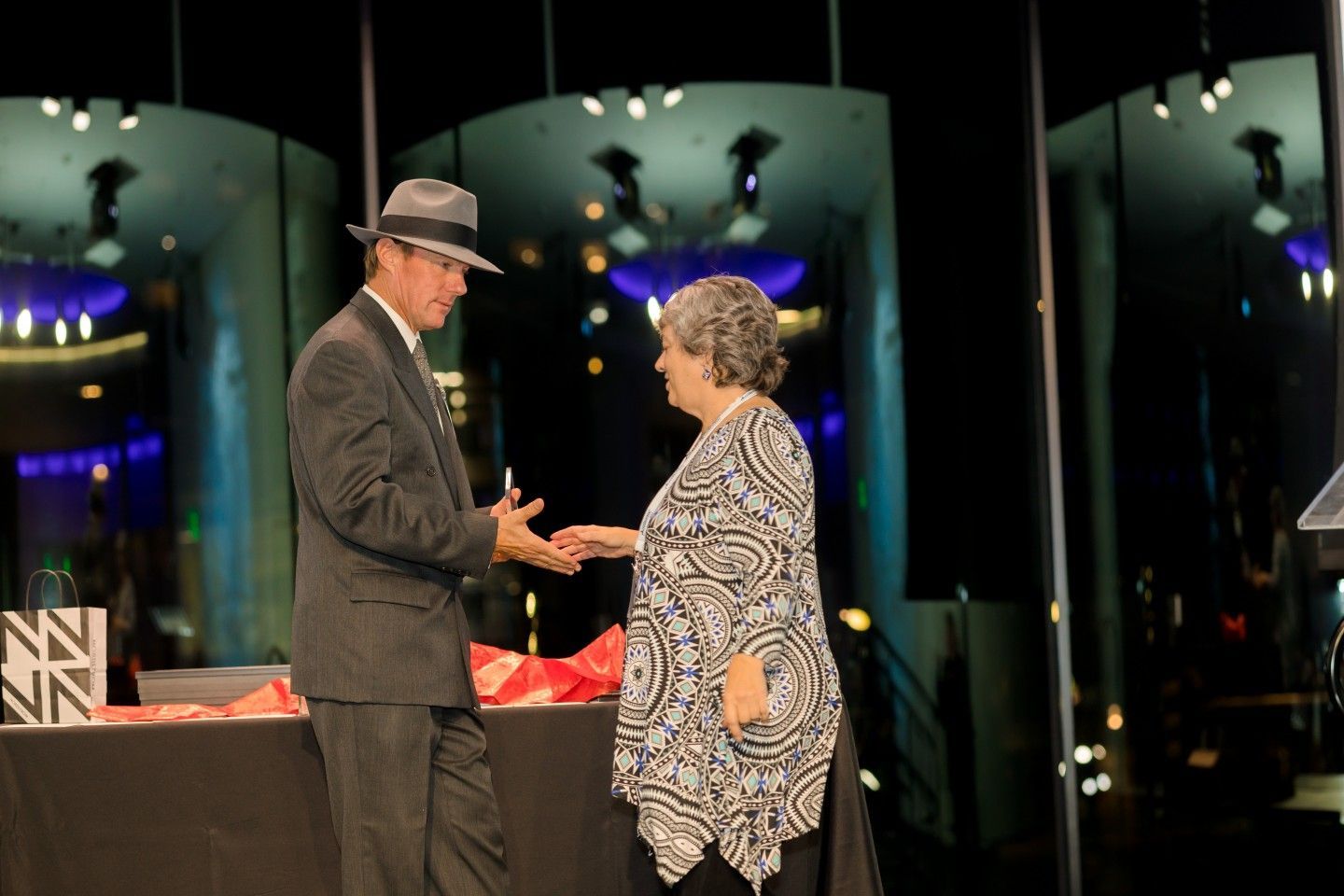 Man in hat hands award to woman, stage background.