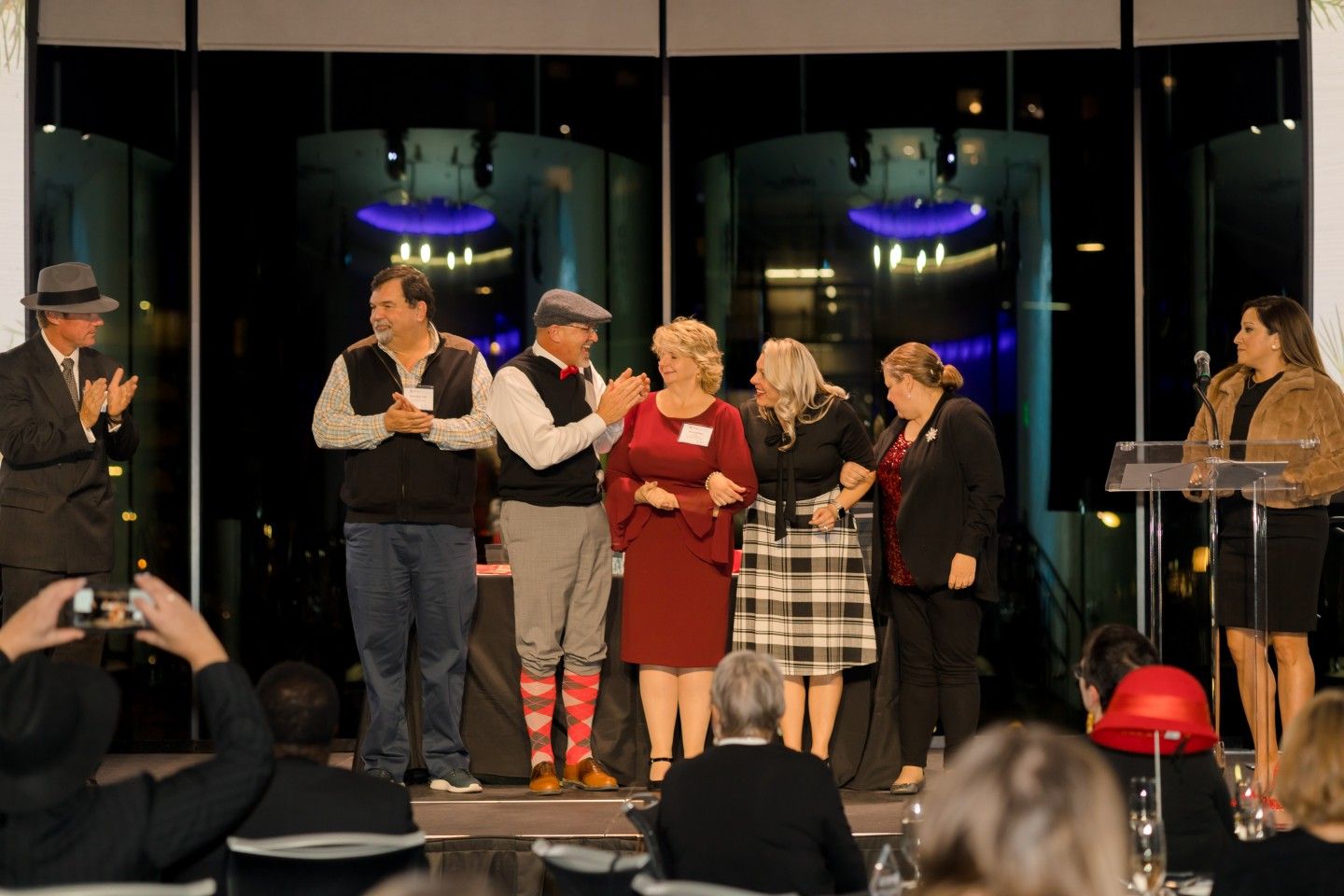 People on stage at an event, with cityscape backdrop. Some applaud, others smile.
